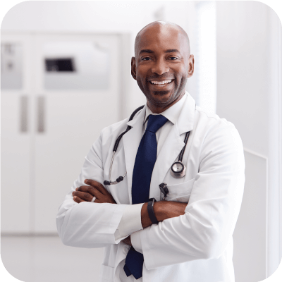 Male doctor smiling with arms crossed in a hospital hallway.